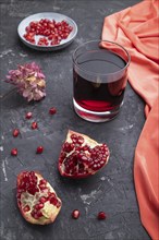 Glass of pomegranate juice on a black concrete background with red textile. Side view, close up