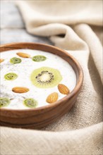 Yogurt with kiwi, gooseberry, chia and almonds in wooden bowl on gray wooden background and linen