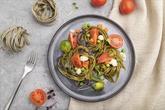 Tagliatelle green spinach pasta with tomato, pea and microgreen sprouts on a gray concrete