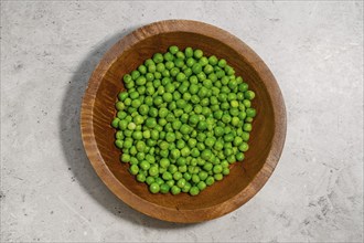 Top view of defrosted fresh green peas in a wooden bowl on a grey stone table