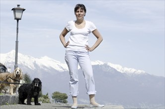 Proud and Elegant Woman Standing with Her Cute Dogs and Snow Capped Mountain in a Sunny Day in