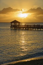 People on a jetty watching the sunset over the sea with beautiful reflection on the water,