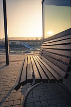 A wooden bench covered with frost in front of a swimming pool at sunrise, ENCW outdoor pool Calw,