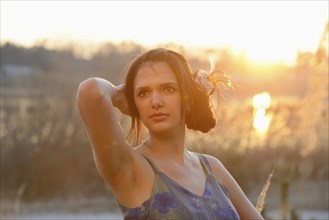 Woman with long hair standing among dry reeds during sunset, looking serene, Bavaria