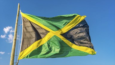 The flag of Jamaica flutters in the wind, isolated against a blue sky