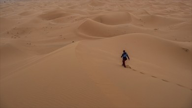 Woman walking over dunes, Erg Chebbi, Sahara, Merzouga, Morocco, Africa