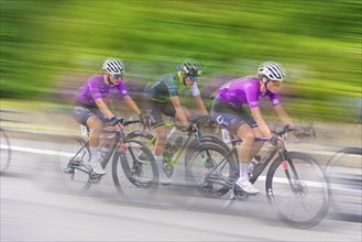 Several cyclists in purple jerseys moving at high speed during a race. Background is blurred and