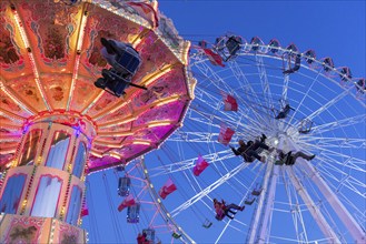 Illuminated chain carousel and Ferris wheel at night with cheerful people, funfair, wave flight,