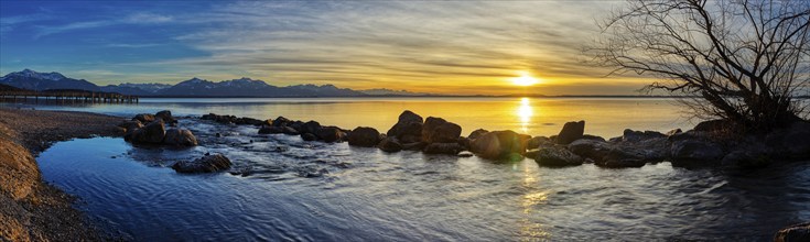 Reflecting sunset scene with mountains and stones on the water at a clear lake, Chiemsee