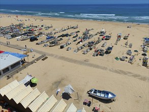 Beach with many boats, huts and parasols. In the background the sea and some beach visitors, aerial