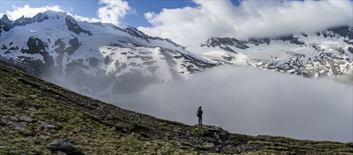 Mountaineer on a rock in front of a mountain landscape, high fog in the valley, panorama with