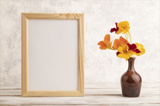 Wooden frame with orange nasturtium flowers in ceramic vase on gray concrete background. side view,