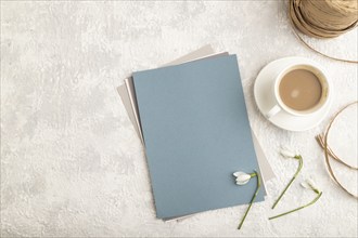 Blue paper sheet mockup with spring snowdrop galanthus flowers and cup of coffee on gray concrete