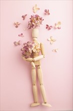 Wooden mannequin holding hydrangea flowers on pink pastel background. close up, isolated, spring,