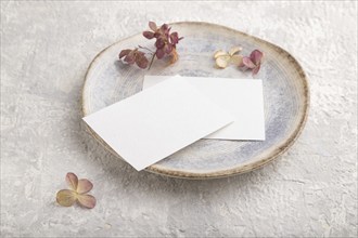 White paper invitation card, mockup with dried hydrangea flowers on ceramic plate and gray concrete