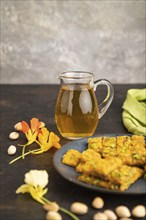 Traditional iranian dessert sohan with glass of green tea on a black concrete background and green