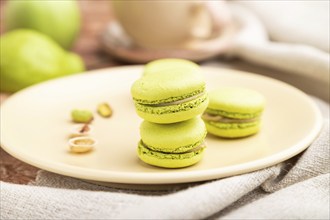 Green macarons or macaroons cakes with cup of coffee on a brown concrete background and linen