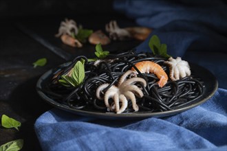 Black cuttlefish ink pasta with shrimps or prawns and small octopuses on black concrete background