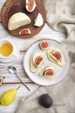 Summer appetizer with pear, cottage cheese, figs and honey on a white wooden background and linen