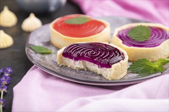 Sweet tartlets with jelly and milk cream with cup of coffee on a black concrete background and pink