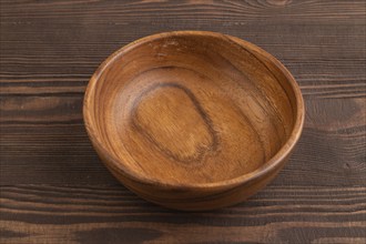 Empty brown wooden bowl on brown wooden background. Side view, copy space