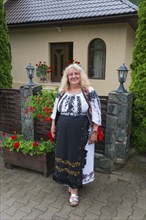 Woman in traditional outfit smiling in front of a house with flowers, Woman in traditional