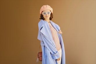 Lovely woman in coral beret and blouse, blue raincoat and sunglasses posing outdoor