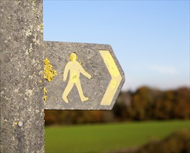 Close up of footpath sign with yellow human figure walking and direction arrow pointing the way,