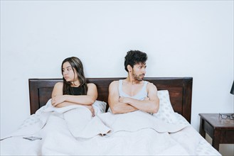 Conflicting couple sitting on bed, Upset couple sitting on bed with crossed arms. Young couple