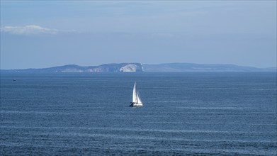 White sailboat at sea with the Isle of Wight in the background, Dorset Coast, Poole, England,