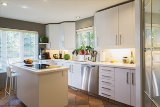 White cabinets, quartz countertop and island with glass cooktop and high back bar stool in kitchen