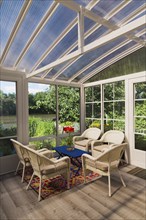 Beige wicker armchairs and blue wooden table in sunroom at back of luxurious residential home,