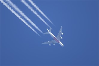 Airbus A380 aircraft of Emirates airlines flying across a blue sky leaving a contrail or vapor