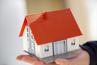 Symbolic image Desire to own a home: woman holding a model house in her hand