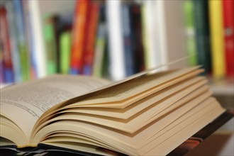 Close-up of an open book, behind it a blurred bookshelf