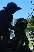 Two childlike figures, butens, angels, as a statue in the shade of a tree in front of a fountain in