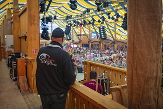 Man in security jumper standing in front of a busy event in a tent, Canstatter Wasen, Stuttgart,