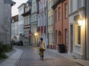 A woman rides a bicycle through a street lit with lanterns in the historic old town of Stralsund,