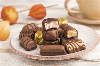 Chocolate candies with cup of coffee and physalis flowers on a white wooden background and orange