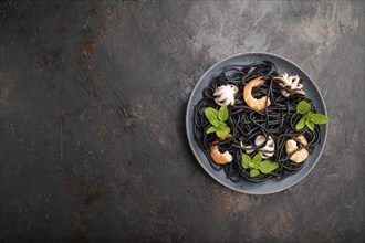 Black cuttlefish ink pasta with shrimps or prawns and small octopuses on black concrete background.