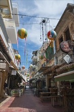 Narrow alley decorated with colourful hanging balloons, surrounded by shops, Kalamata, Messinia,