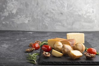 Smoked cheese and various types of cheese with rosemary and tomatoes on black slate board on a