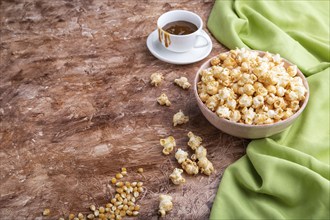 Popcorn with caramel in ceramic bowl on brown concrete background and green textile. Side view,