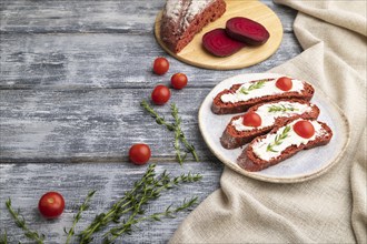 Red beet bread sandwiches with cream cheese and tomatoes on gray wooden background and linen