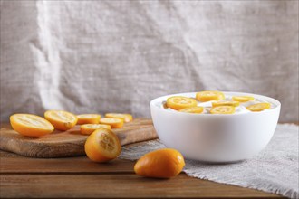 Greek yogurt with kumquat pieces in a white plate on a brown wooden background, close up