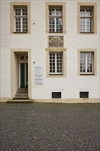 Facade of a historic building with white windows, door and a colourful family coat of arms in the