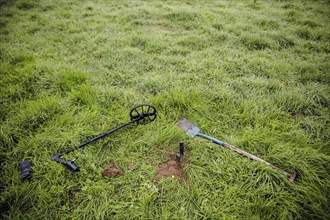 Symbolic photo on the subject of treasure hunting. A metal detector and a spade lie in a meadow.