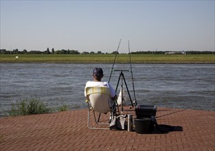 Man sitting alone fishing in the River Maas at Ablasserdam, Netherlands