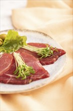 Slices of smoked salted meat with cilantro microgreen on gray concrete background and orange