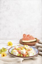 Vegetarian salad with watermelon, feta cheese, and grapes on blue ceramic plate on white wooden